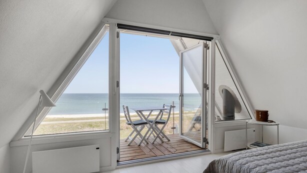 Ein Schlafzimmer mit großem Fenster und Meerblick, ein Bett, ein Sessel und ein kleiner Tisch.