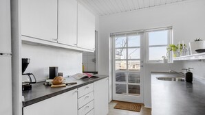 Eine moderne Küche mit weißen Schränken, einer Kaffeemaschine, einem Brotlaib und einem Fenster mit Blick ins Freie.