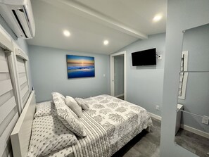 A bedroom with a bed, a painting, a television, and an air conditioning unit.