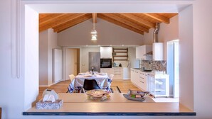A modern kitchen with wooden beams, a dining area with a table set for two, and a kitchen counter with a coffee machine. - Cozy home in Albagnano di Bee with house sea view (Albagnano di Bee)