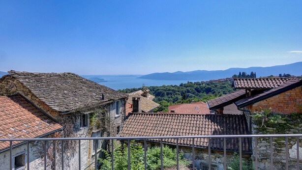 A view of terracotta-roofed buildings with stone walls, overlooking a body of water and distant mountains. - Cozy home in Albagnano di Bee with house sea view (Albagnano di Bee)