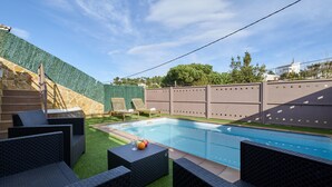 Una piscina con mobiliario de mimbre alrededor y una pared de piedra.
