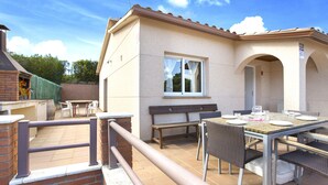 Un patio con una mesa y sillas, una parrilla de barbacoa y una ventana con vista a un jardín.