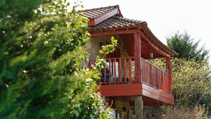 Un edificio in pietra con un balcone rosso e un tetto in tegole, immerso nel verde.