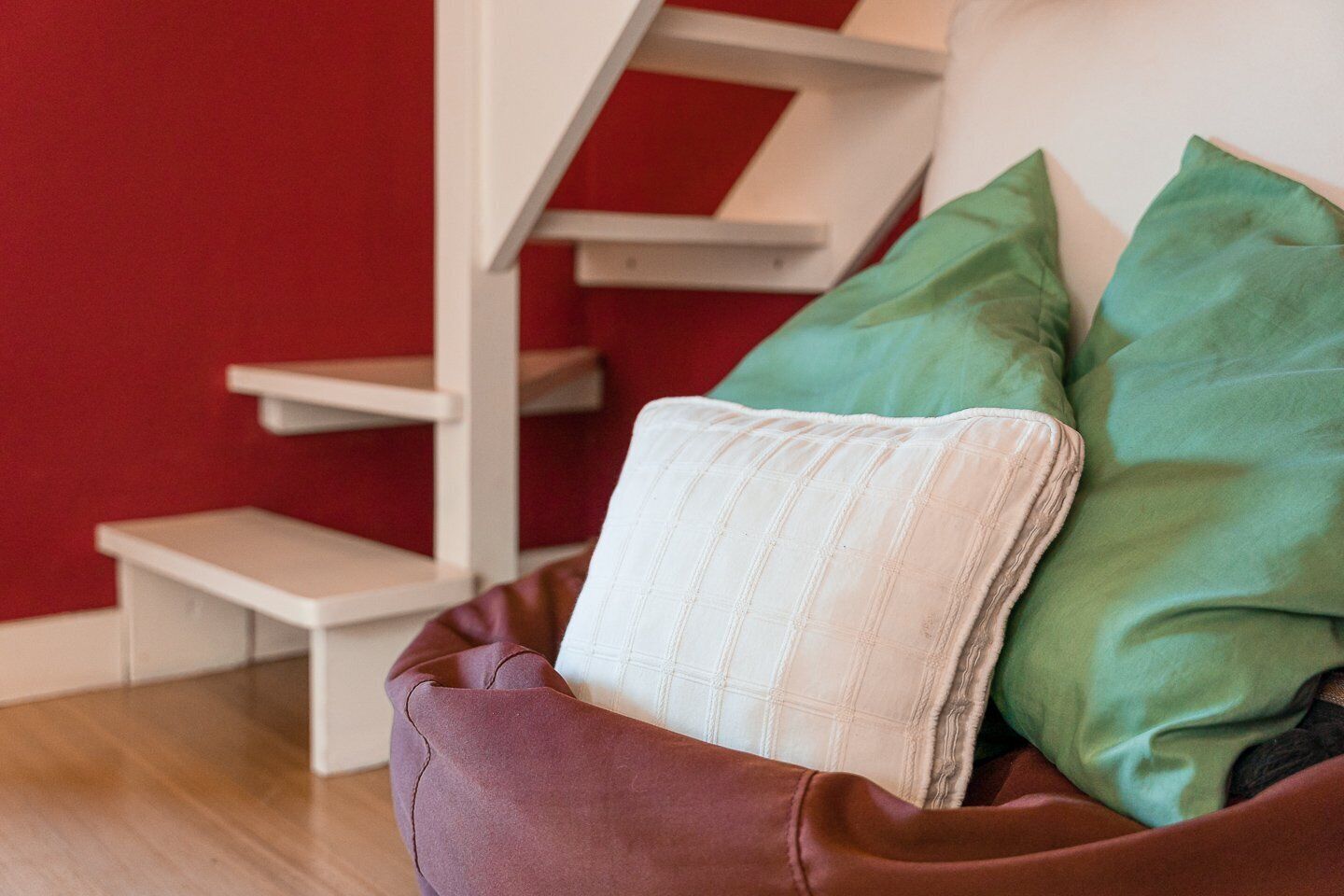 Eine rote Wand, eine Treppe und ein brauner Sessel mit weißem Kissen und grünen Zierkissen.