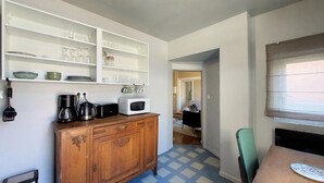 Een kleine keuken met witte planken, een houten kastje, een magnetron en een koffiezetapparaat.