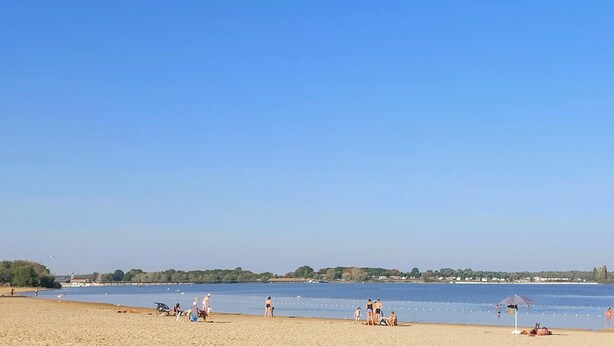 Een strand met mensen, een heldere lucht en een rustig waterlichaam.