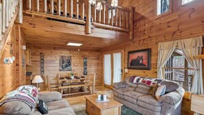 A wooden cabin interior with a dining area, a sofa, and a staircase. - Mountain views, HUGE theater room, hot tub, game room! (Sevierville)