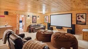 A cozy room with a wooden ceiling, a large screen, a brown leather sofa, and a bean bag. - Mountain views, HUGE theater room, hot tub, game room! (Sevierville)