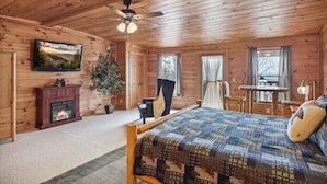 A wooden cabin bedroom with a bed, a fireplace, a ceiling fan, and a television on the wall. - Mountain views, HUGE theater room, hot tub, game room! (Sevierville)