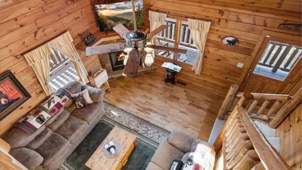 A log cabin interior with a fireplace, a ceiling fan, a sofa, and a coffee table. - Mountain views, HUGE theater room, hot tub, game room! (Sevierville)