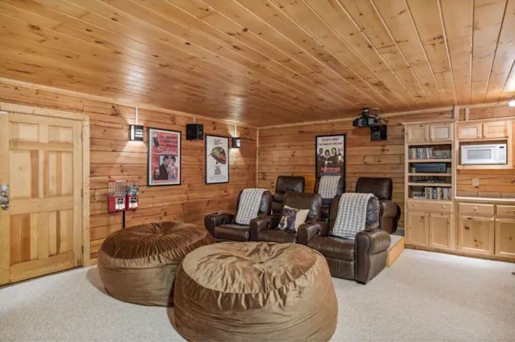 Interior acolhedor de uma cabana com paredes e teto de madeira, poltronas reclináveis de couro e um grande puff.