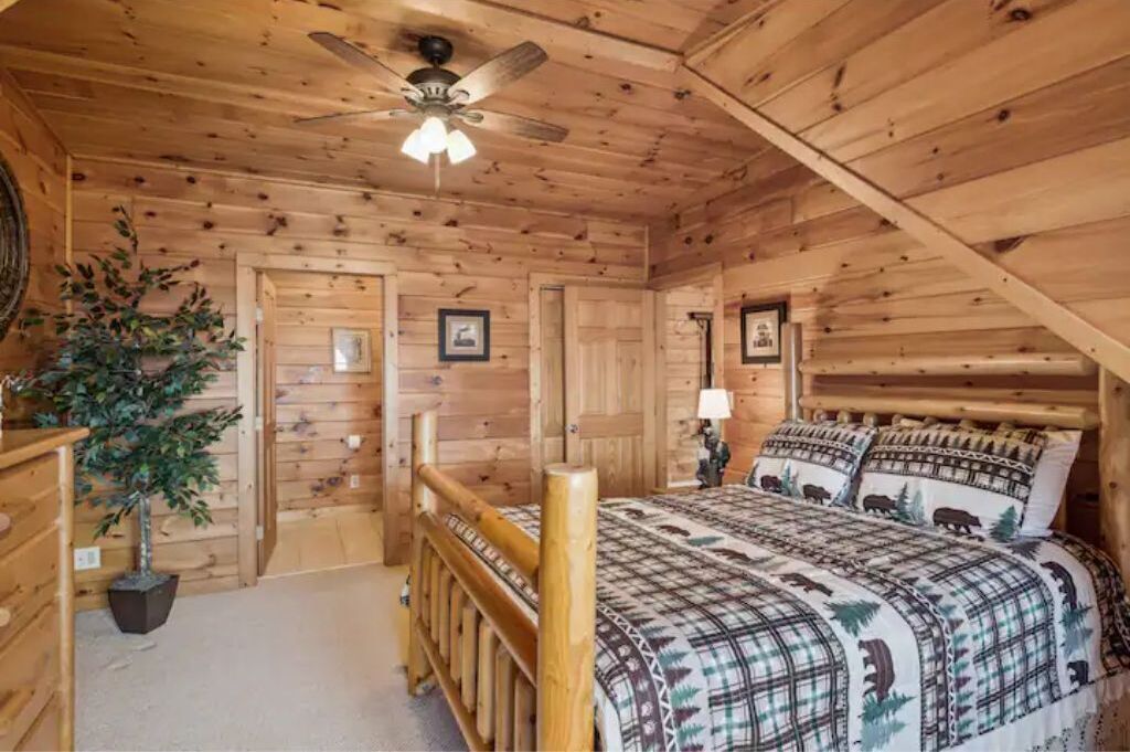 Une chambre dans une cabane en bois, avec un lit, un ventilateur de plafond et une plante en pot.