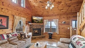 A cozy cabin interior with a fireplace, wooden walls, and a comfortable seating area. - Mountain views, HUGE theater room, hot tub, game room! (Sevierville)