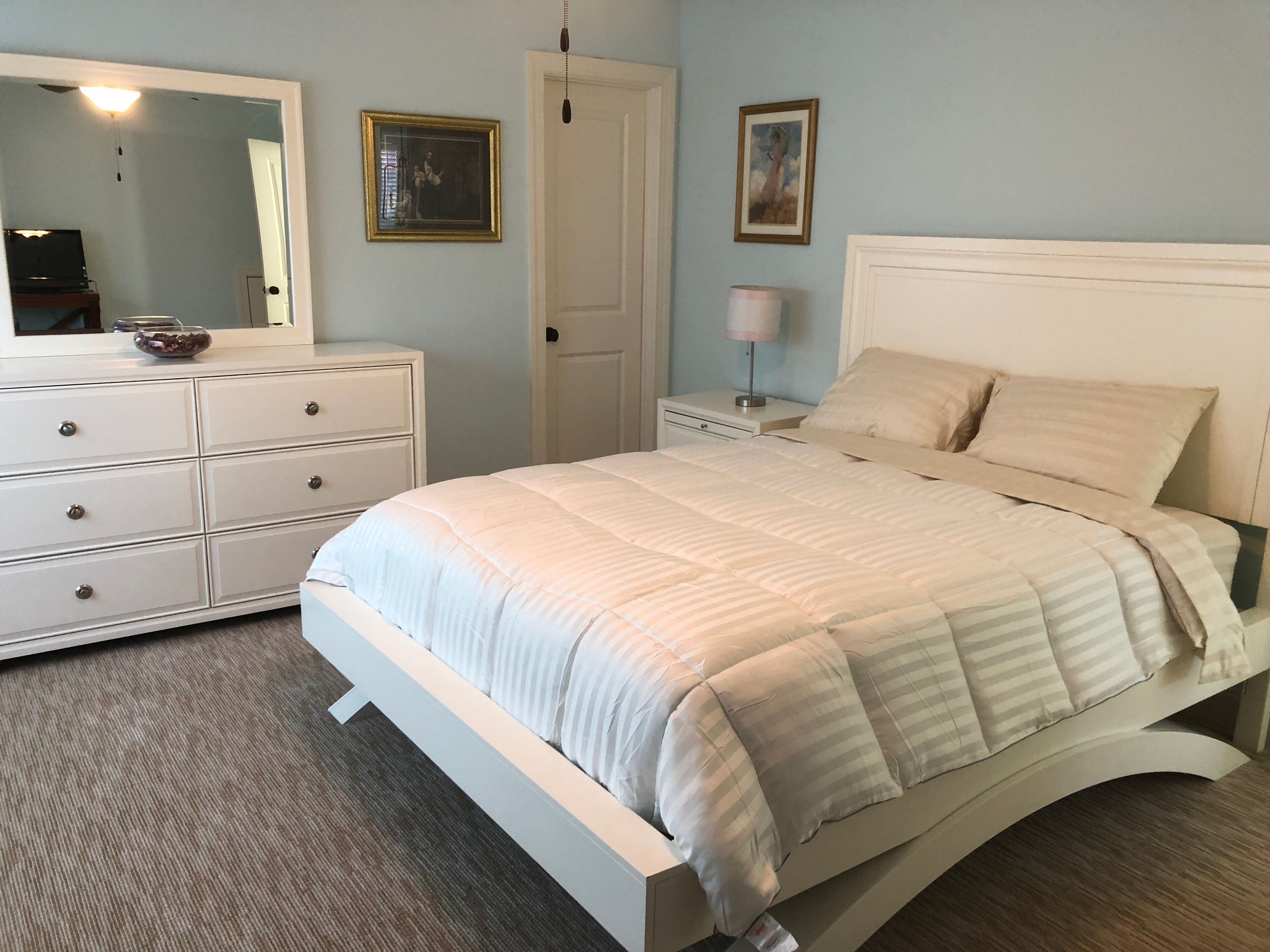 A bedroom with a bed, dresser, nightstand, and two framed pictures on the wall.