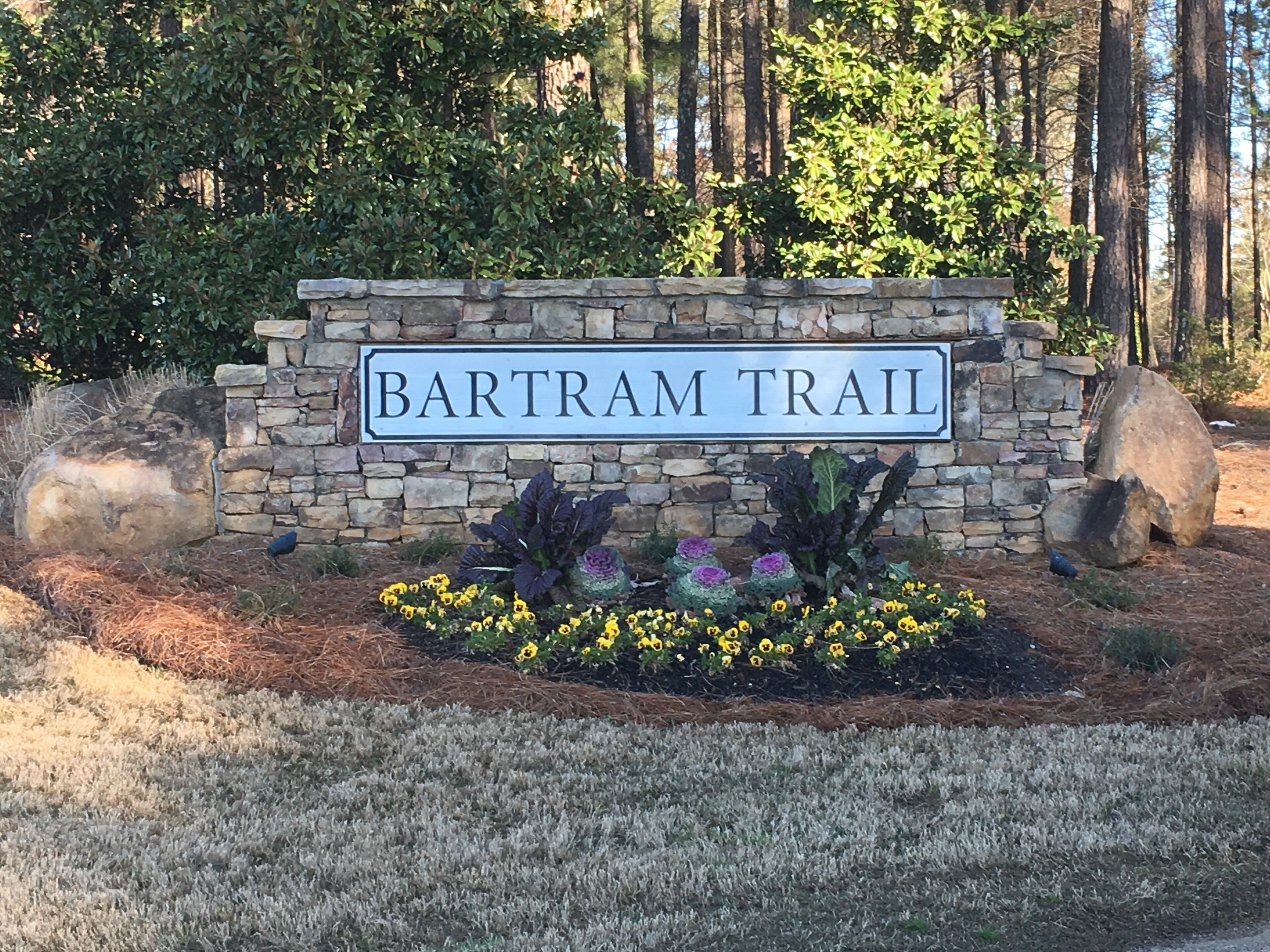 Ein Steinschild mit der Aufschrift 'BARTRAM TRAIL', umgeben von einer begrünten Fläche mit Steinen und Blumen.