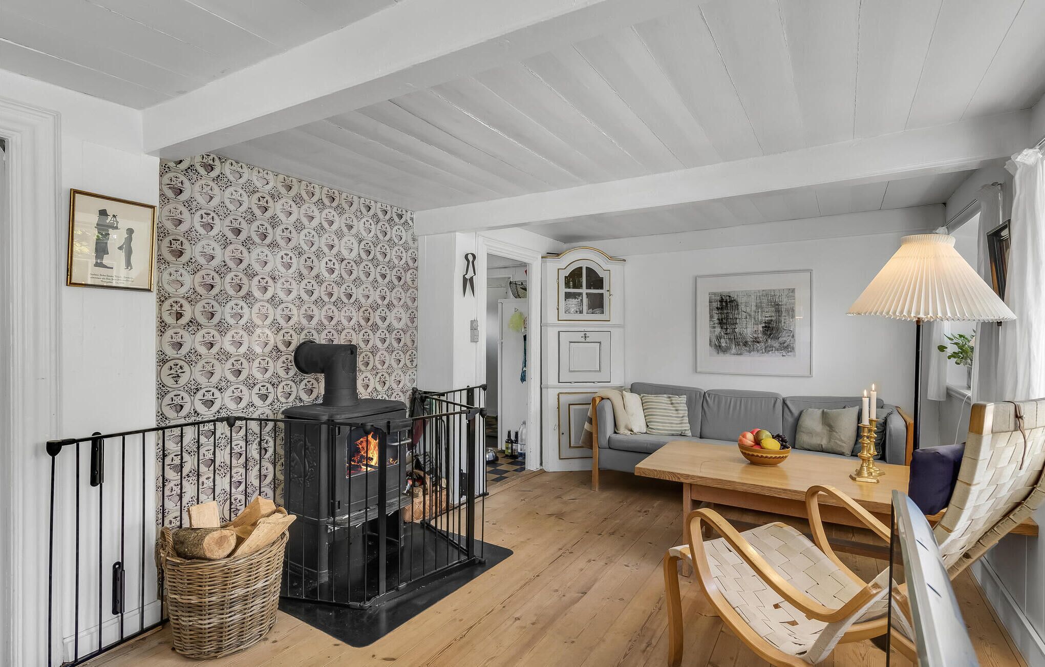 A cozy living room with a fireplace, a grey sofa, a wooden dining table, and a wicker basket.