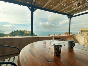 A wooden table with two mugs and a glass, set on a balcony with a view of the sea and buildings. - Papou cottage (Pelekas)