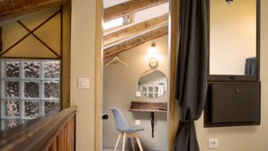 Ein Zimmer mit Holzbalkendecke, einem Spiegel, einem Sessel und einer Pendelleuchte.