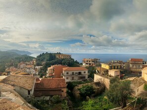 A coastal town with terracotta-roofed buildings, a hillside with greenery, and a view of the sea. - Papou cottage (Pelekas)