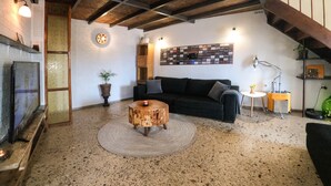 Ein gemütliches Wohnzimmer mit Kamin, einem runden Holztisch, einer schwarzen Couch und einem an der Wand befestigten Bilderrahmen.