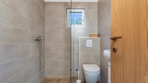 Une salle de bain moderne avec une douche à parois de verre, des toilettes et une petite fenêtre.