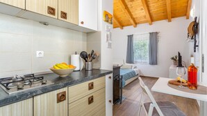 Une cuisine compacte avec une cuisinière à gaz, un saladier de fruits et un évier. On y trouve également un petit coin repas avec une table, une chaise et une bouteille de vin.