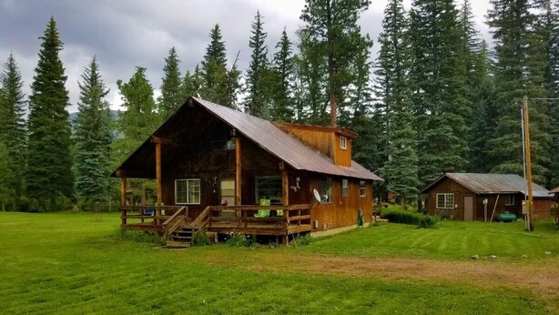 A rustic cabin with a porch, surrounded by a lush green field and dense forest. - Dog Friendly Creekside Property close to Vallecito Lake minutes to Durango (Bayfield)