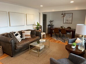 Relax in a stylish living room with a leather sofa, coffee table, and armchair, surrounded by artwork and a potted plant.