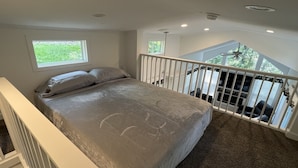 Een slaapkamer met een groot bed, een raam, een balkon met een hekwerk en een plafondventilator.