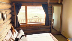 Une chambre dans une cabane en rondins, avec un lit, une fenêtre avec des rideaux et une porte en bois.