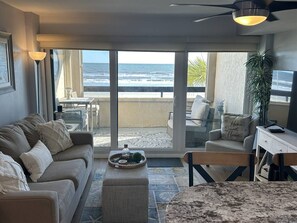 Ein Wohnzimmer mit einer Couch, Couchtisch und einem Essbereich mit Tisch und Stühlen. Ein großes Fenster bietet Blick auf den Ozean.