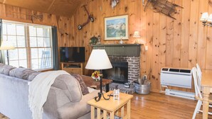 A cozy living room with a fireplace, wooden walls, a sofa, a TV, and a lamp. - Bayberry Cottage  (Lexington)