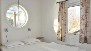 A bedroom with a bed, a round window, a wall-mounted lamp, and a window with floral curtains. - Awesome home in åmotfors with WiFi (Åmotfors)