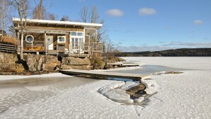 A lodge with a wooden exterior, a covered deck, and a view of a frozen lake. - Awesome home in åmotfors with WiFi (Åmotfors)