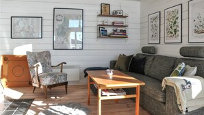A cozy living room with a wooden floor, a patterned armchair, a wooden coffee table, a grey sofa, and a bookshelf with various items. - Awesome home in åmotfors with WiFi (Åmotfors)