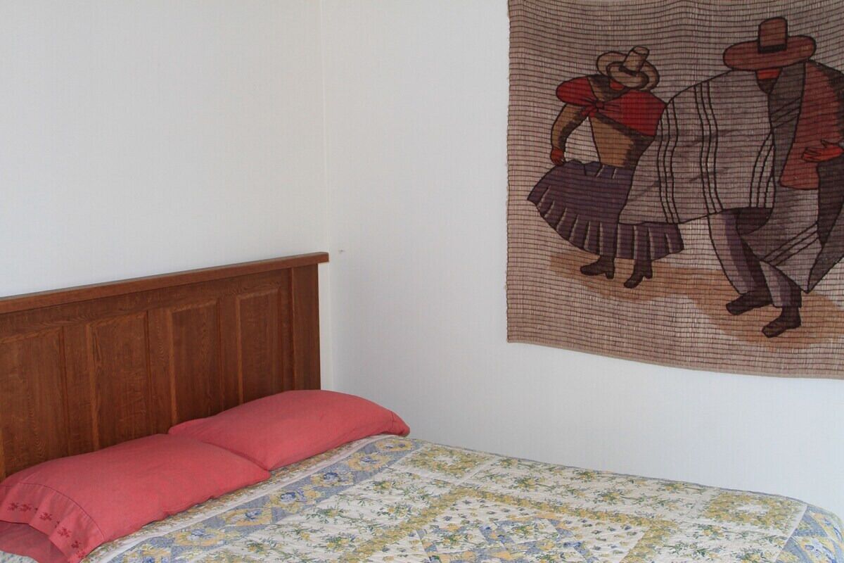 Un dormitorio con cabecera de madera, colcha con estampado floral y un tapiz que representa a una pareja.
