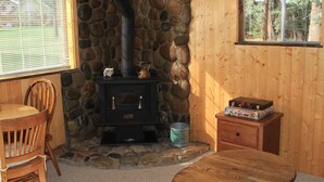 A cozy room with a stone fireplace, a wooden table, a chair, and a window with a view of trees. - Dog Friendly Creekside Property close to Vallecito Lake minutes to Durango and so much adventure out the front door (Bayfield)