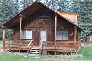 Une cabane en bois rustique, dotée d’un porche à l’avant, d’une porte et de deux fenêtres.