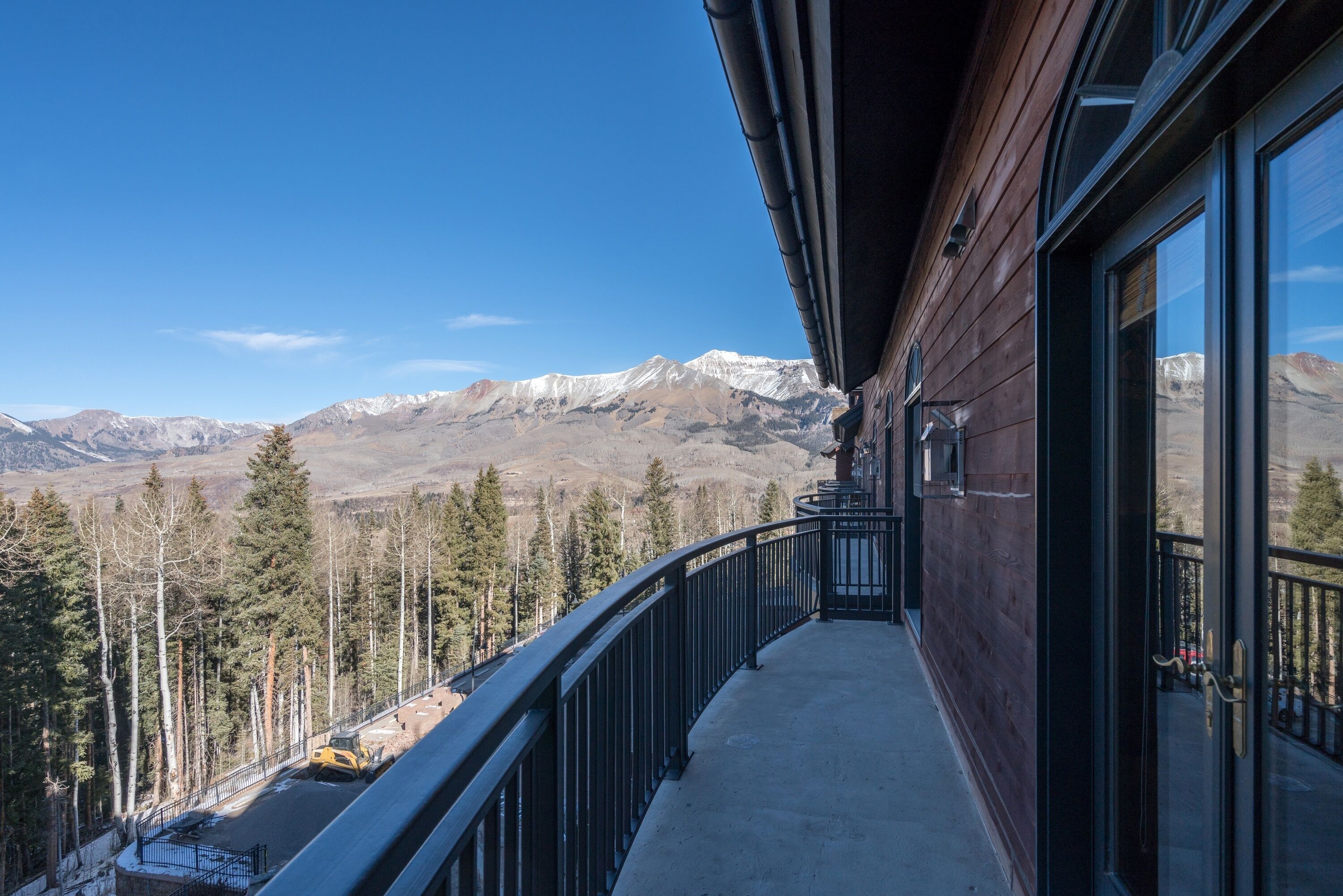 A balcony with a view of snow-capped mountains, a wooden building, and a forested area.