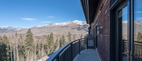 A balcony with a view of snow-capped mountains, a wooden building, and a forested area.