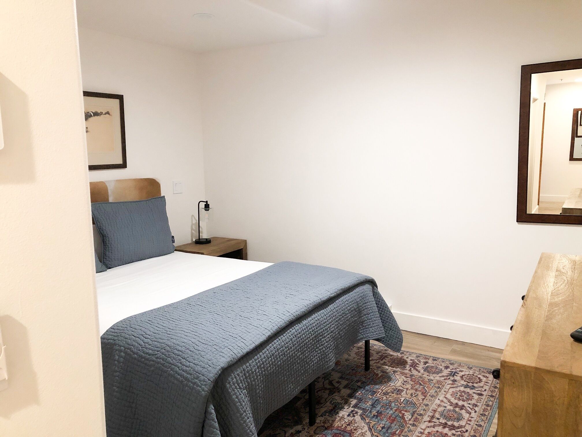 A bedroom with a bed, a nightstand, a lamp, a rug, and a wooden cabinet.