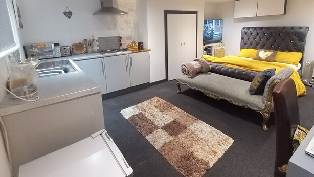 A compact bedroom with a bed, bedside table, and a small kitchenette.