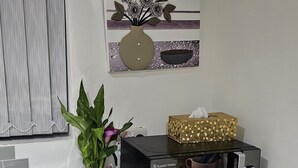 A kitchen with a microwave, a potted plant, a vase with flowers, and a painting on the wall.