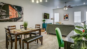 A dining area with a wooden table and chairs, a bench, and a green chair. There is a painting on the wall and a ceiling fan. - 4010 · Comfortable New Home with community pool and golf (Las Cruces)
