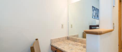 A bathroom with a granite countertop, wooden chair, and a large mirror.