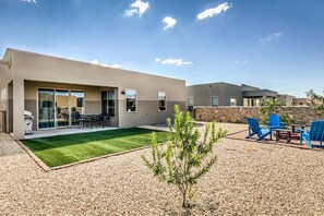 A modern house with a patio, outdoor seating, and a small lawn.