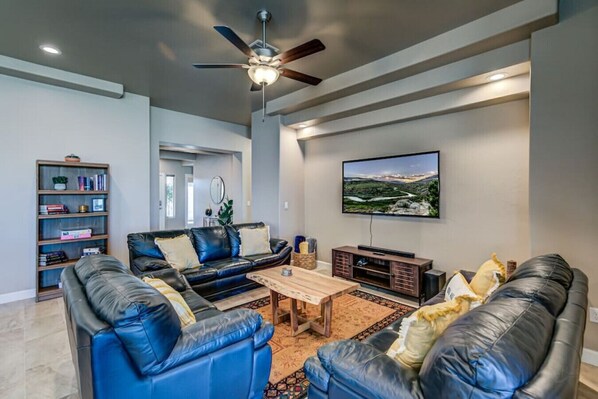 A living room with a black leather sofa, a wooden coffee table, a television, and a bookshelf.