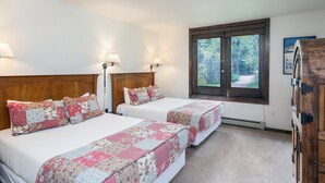 A bedroom with two beds, a wooden headboard, a window with a view of trees, and a wooden cabinet. - Manitou Lodge 2 Hotel Room by Alpine Lodging Telluride (Telluride)