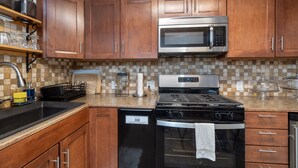 A kitchen with wooden cabinets, a stainless steel microwave, a gas stove, and a dishwasher. - Manitou Lodge 2 Hotel Room by Alpine Lodging Telluride (Telluride)